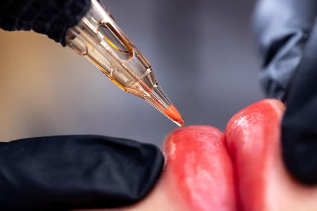 Macro photo of process of applying permanent makeup tattoo of red on lips woman